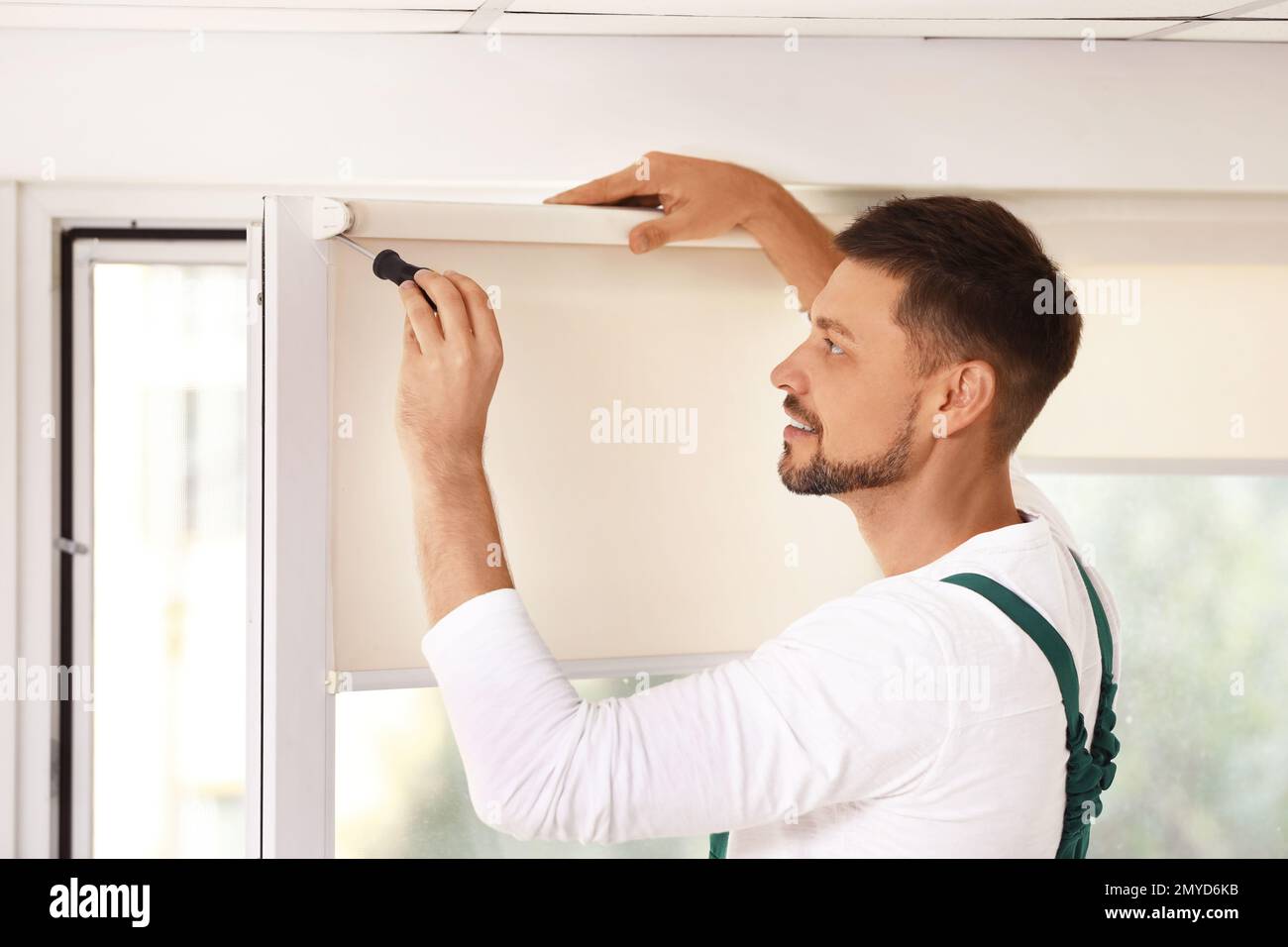 Handyman with screwdriver installing roller window blind indoors Stock Photo