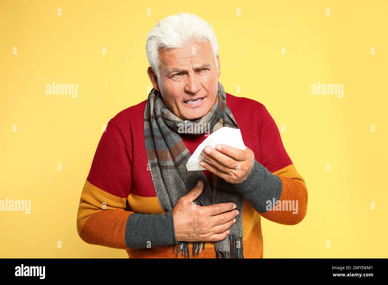 Senior man coughing on yellow background. Cold symptoms Stock Photo