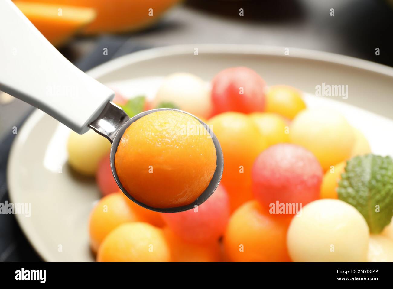Scoop with melon ball near plate of fruit salad, closeup Stock Photo