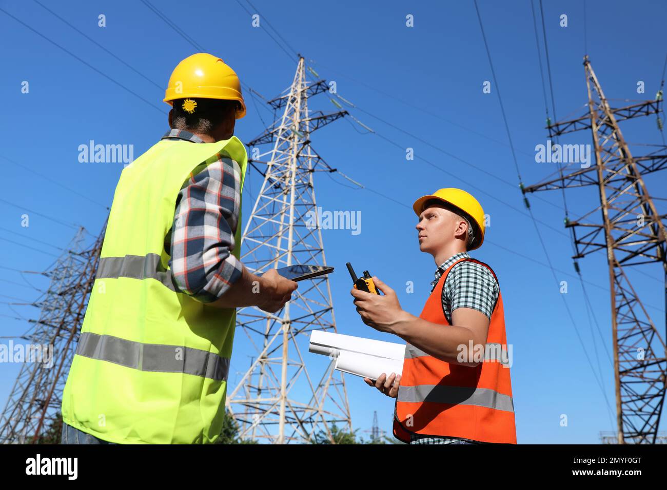 Professional electricians in uniforms near high voltage towers Stock