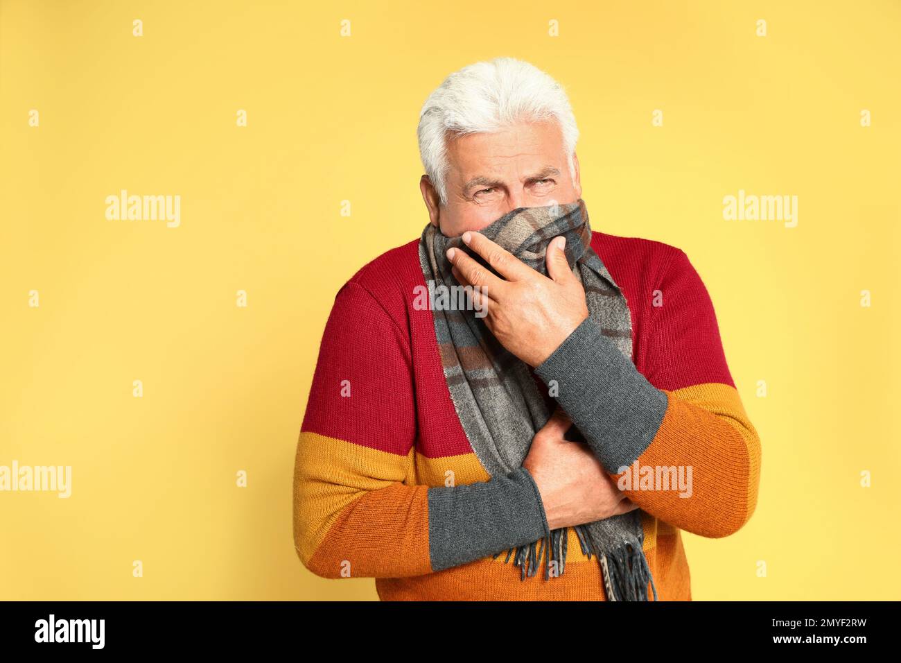 Senior man suppressing cough on yellow background. Cold symptoms Stock Photo