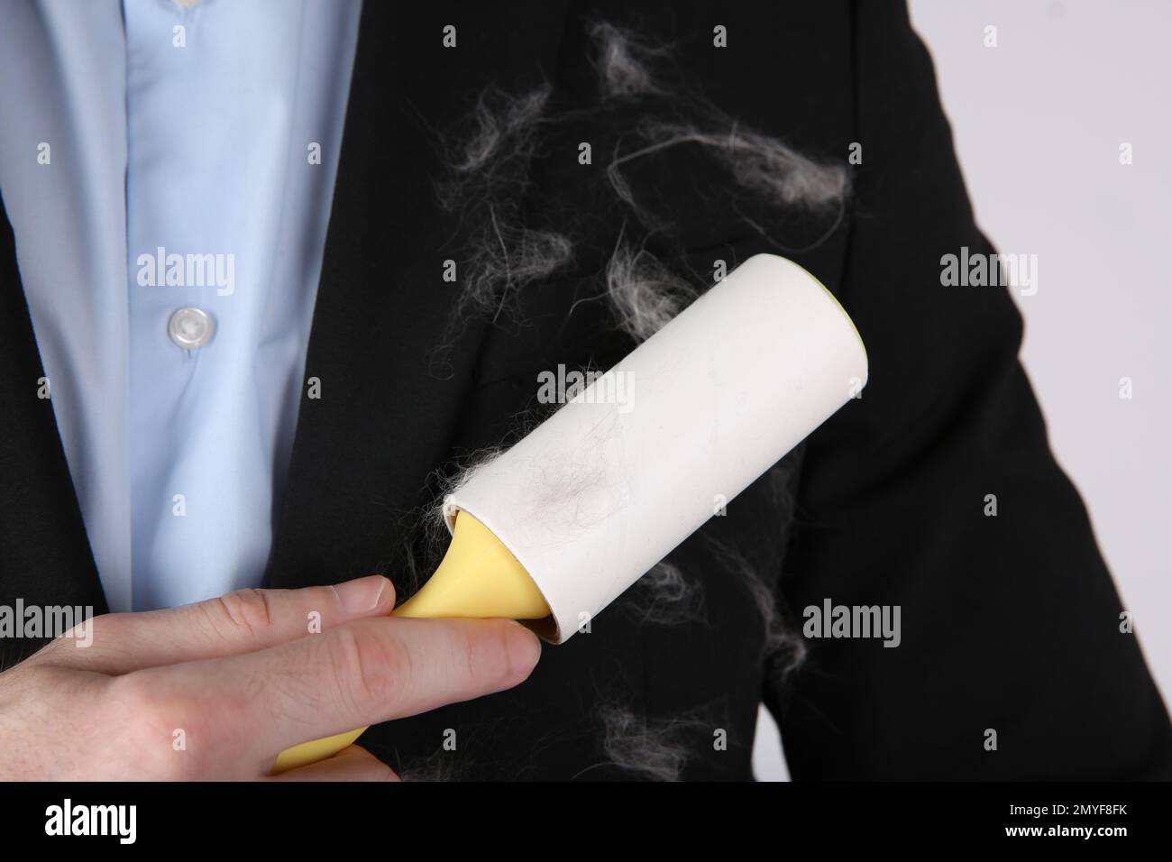 Man removing hair from black jacket with lint roller on light grey