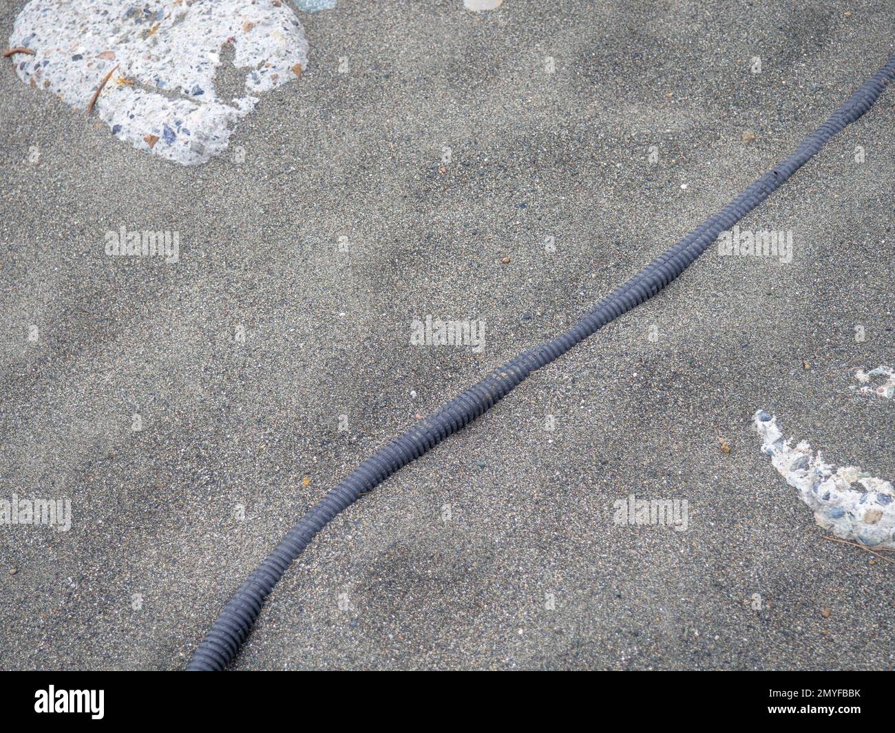 Cable on black sand. The cable sticks out of the ground. Electrical
