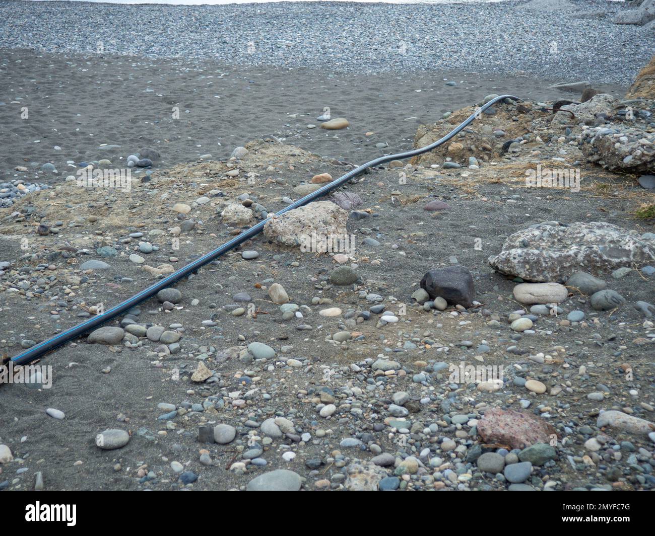 Cable on black sand. The cable sticks out of the ground. Electrical