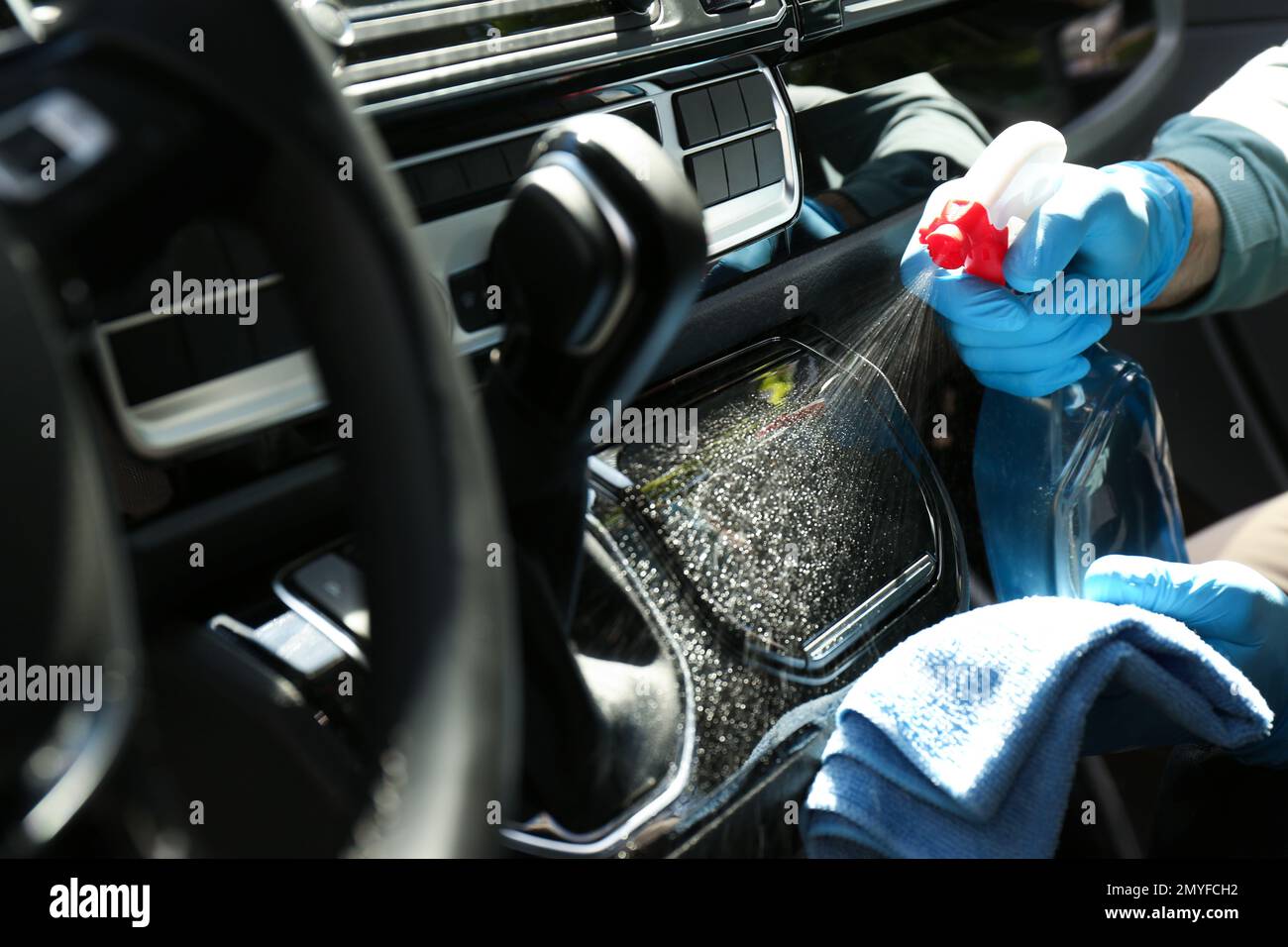 Man in gloves cleaning car dashboard with disinfectant spray and rag