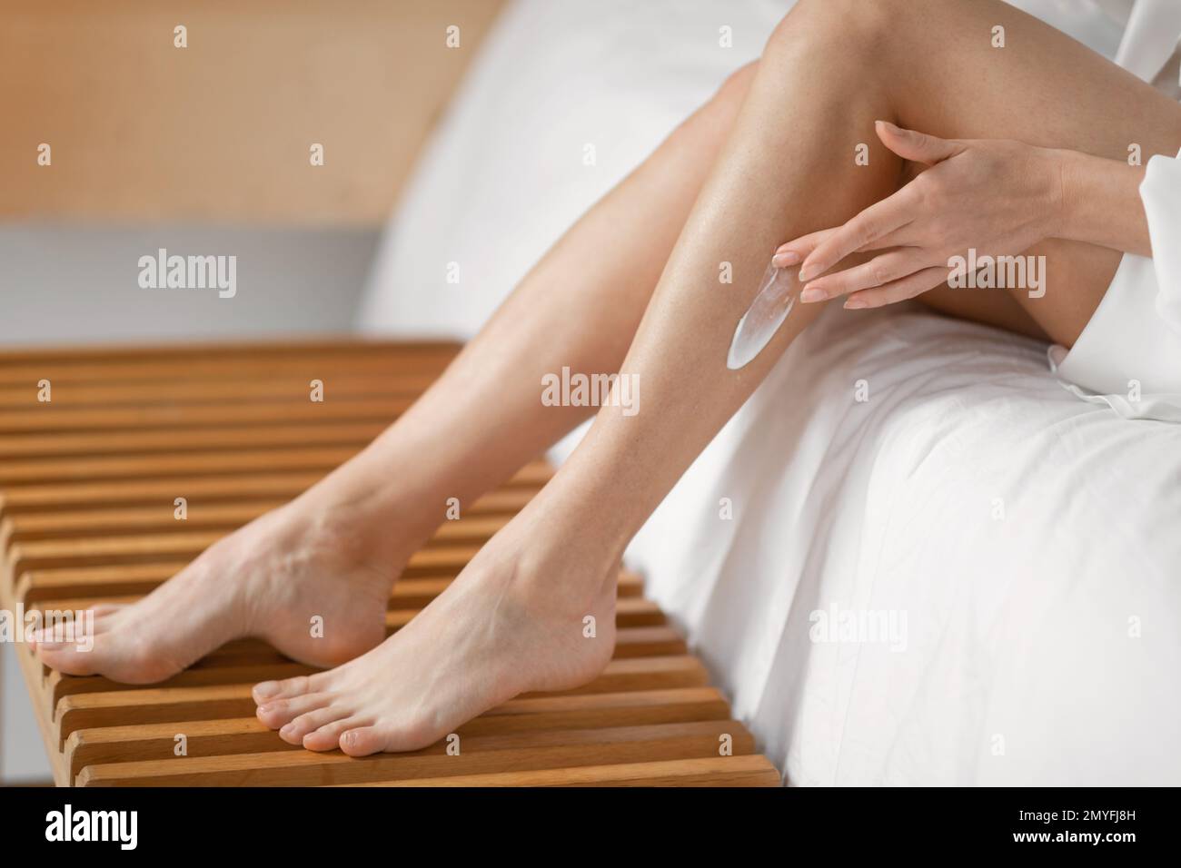 Millennial european woman applies cream on her legs, enjoys daily procedures in bedroom interior alone Stock Photo