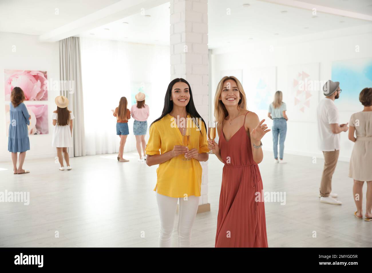 Young women with glasses of champagne at exhibition in art gallery ...