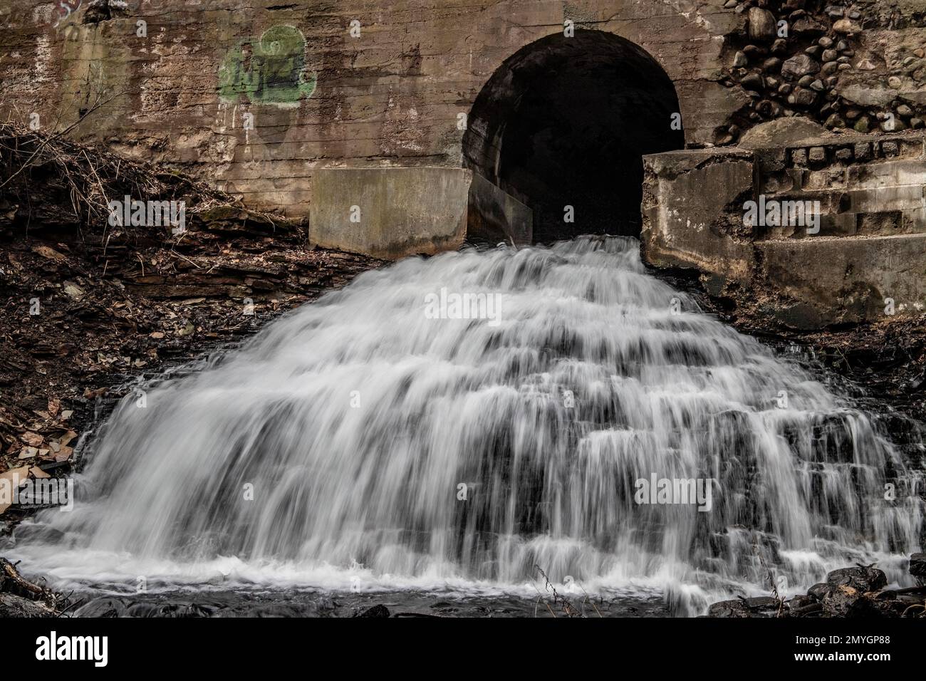 Long exposure waterfall that flows through a tunnel underneath a roadway on a spring day in downtown Marine on St. Croix, Minnesota USA. Stock Photo