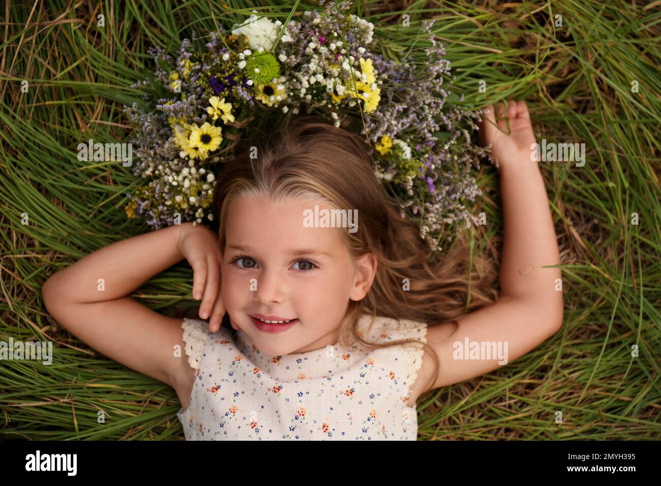 Cute little girl wearing wreath made of beautiful flowers on green ...