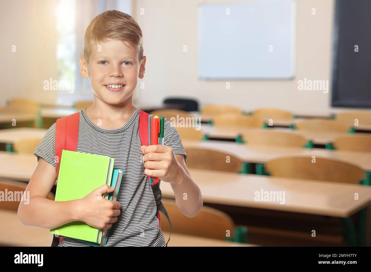 Little boy with school stationery in empty classroom Stock Photo Alamy