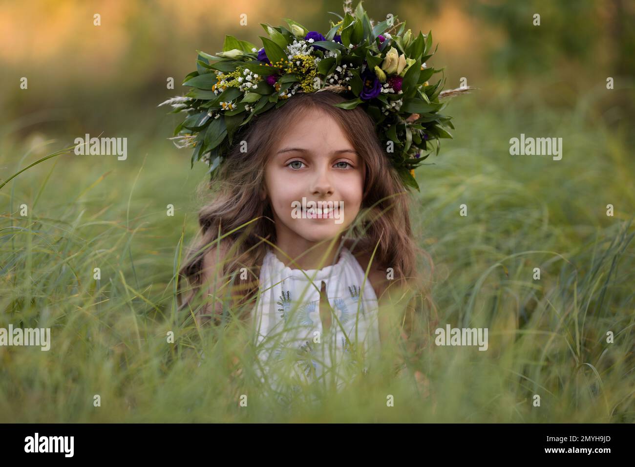 Cute little girl wearing wreath made of beautiful flowers in field ...