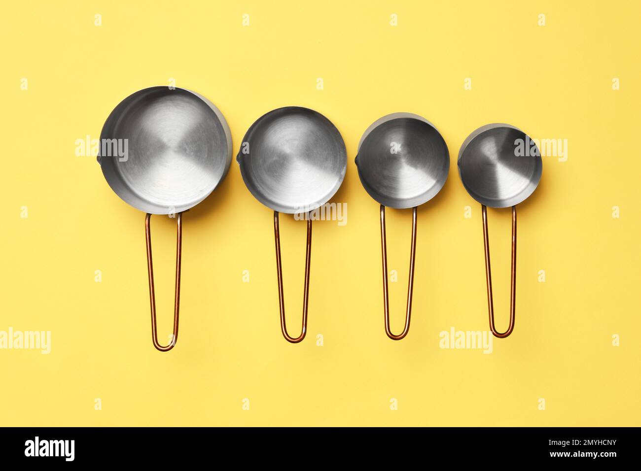 Different saucepans on yellow background, flat lay. Cooking utensils