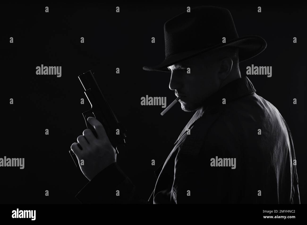 Old fashioned detective with gun smoking cigarette on dark background