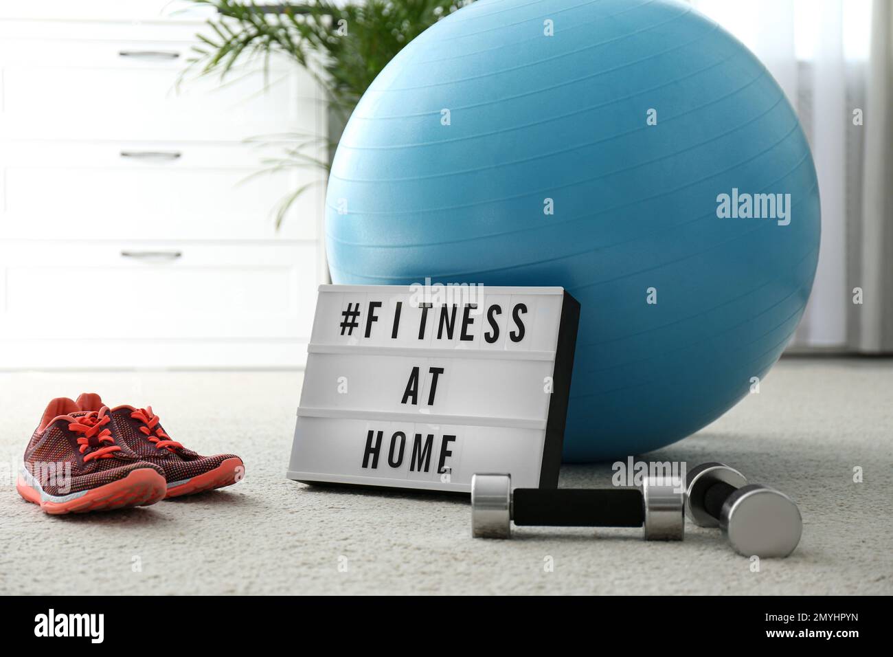 Sport equipment and lightbox with hashtag FITNESS AT HOME on floor indoors.  Message to promote self-isolation during COVID‑19 pandemic Stock Photo -  Alamy