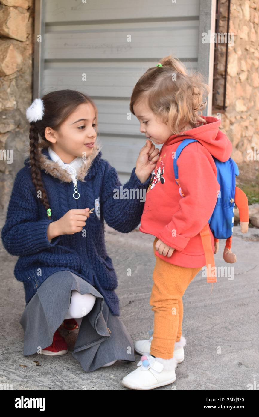 A school girl in northern Iraq shares candy with her little sister. Stock Photo