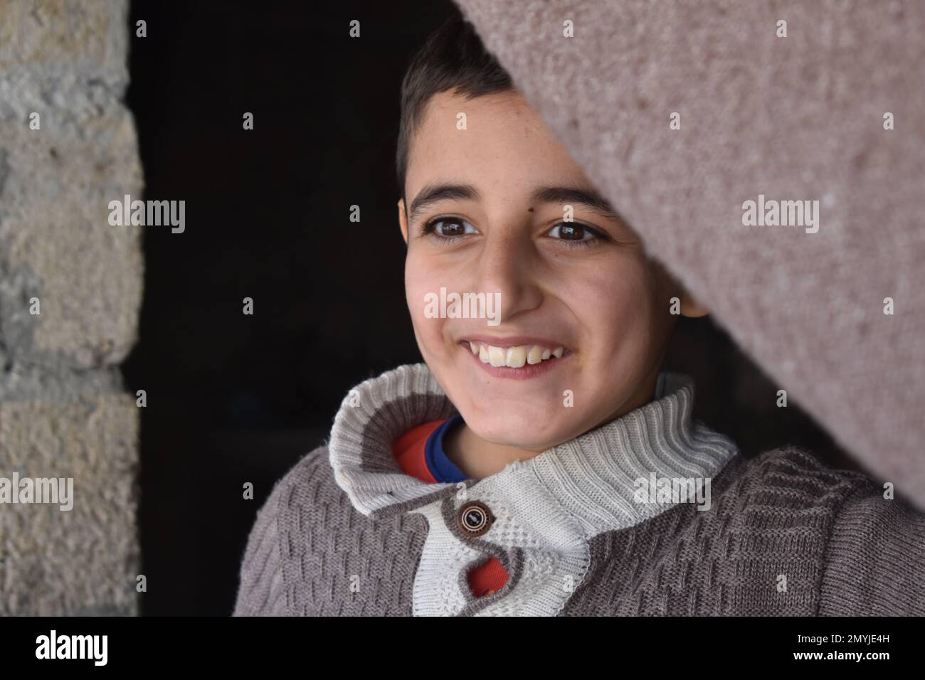 A smiling and dimpled boy holds back the blanket that serves as the ...