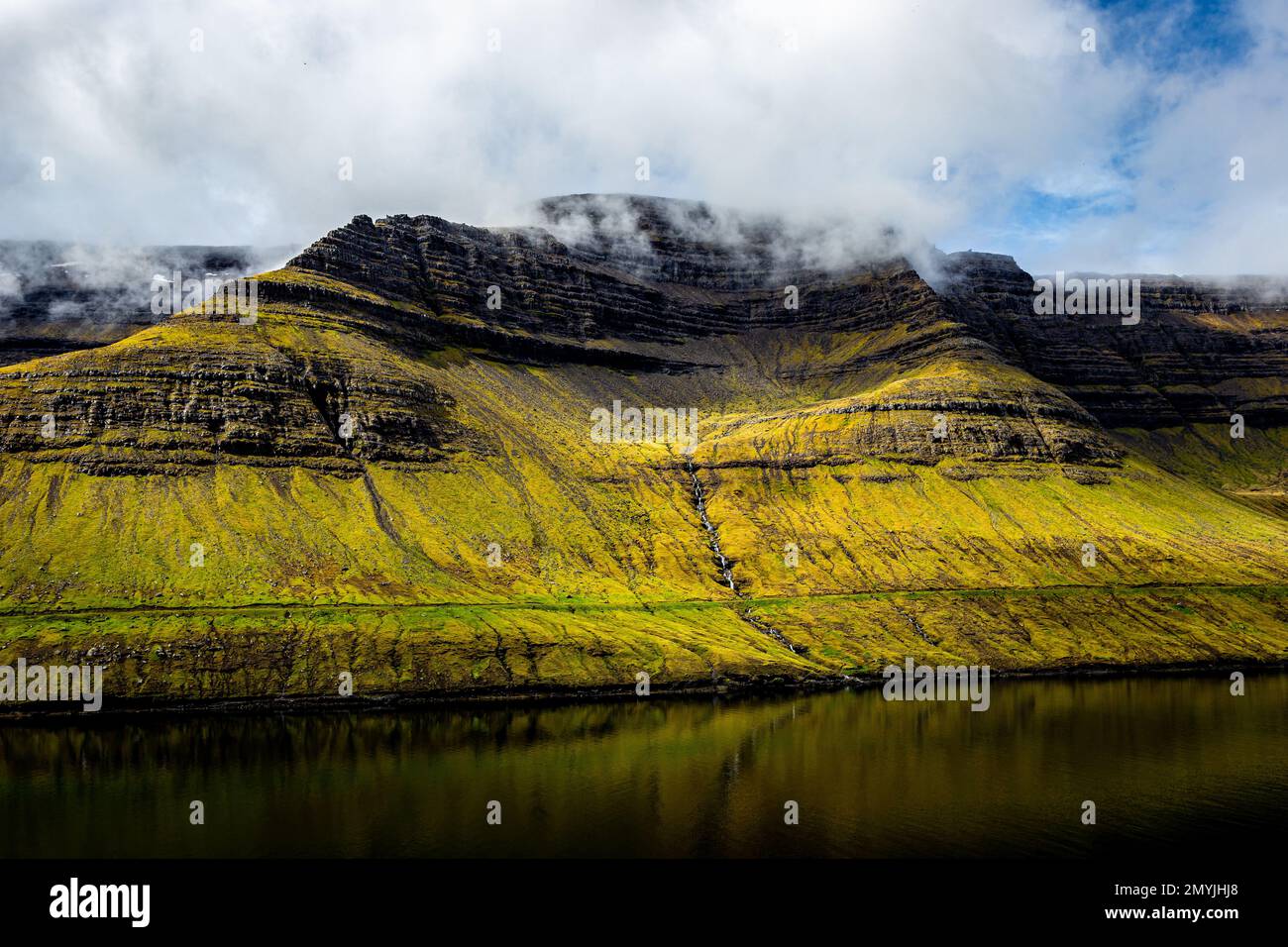 Mountainside stream on Bordoy, Faroe Islands viewed from across a fjord with coastal mountains Stock Photo