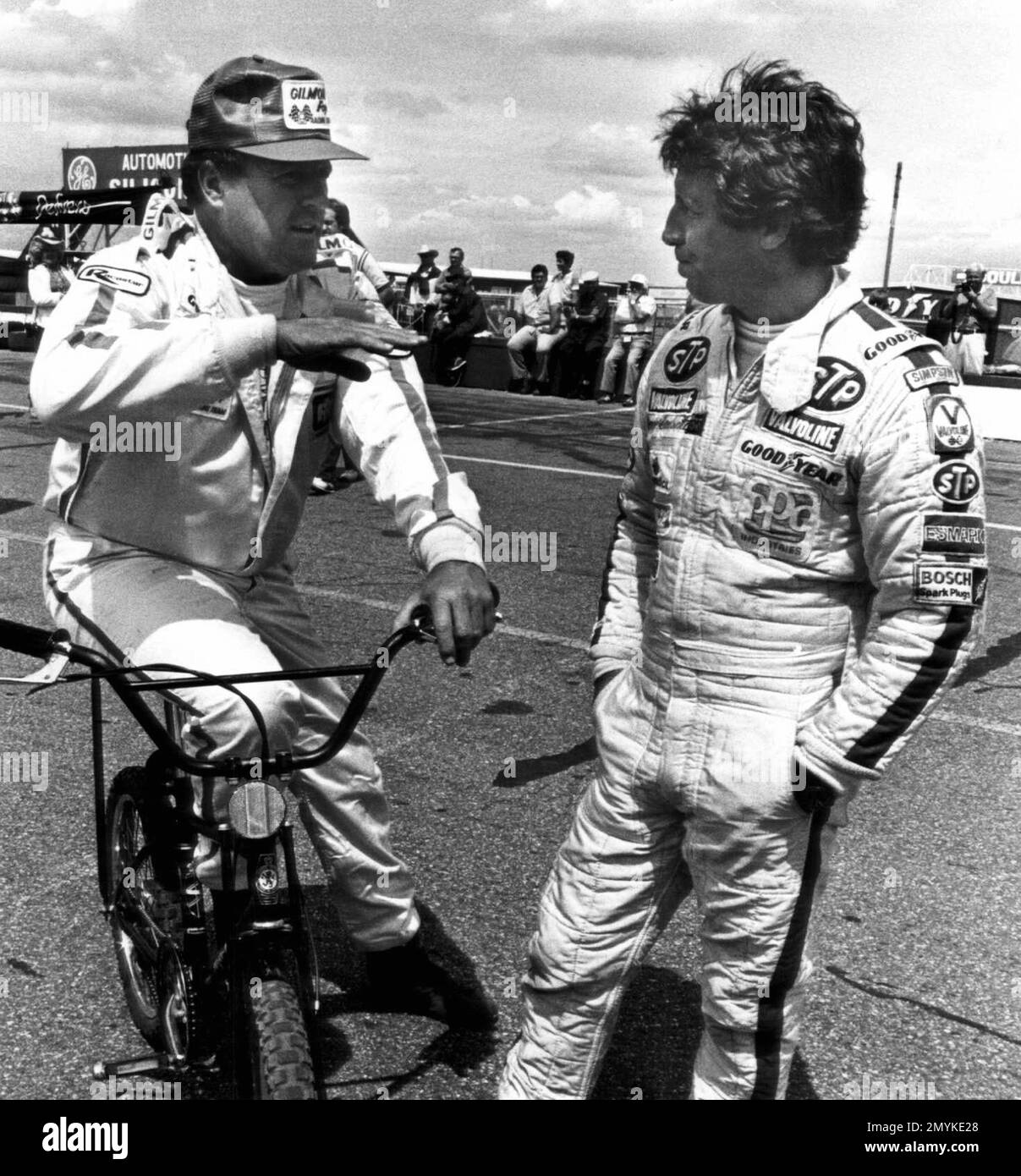 FILE - In this Aug. 14, 1982, file photo, A.J. Foyt, left, of Houston,  Tex., sits on his bicycle talking with Mario Andretti of Nazareth, Pa.,  during a break in practice runs