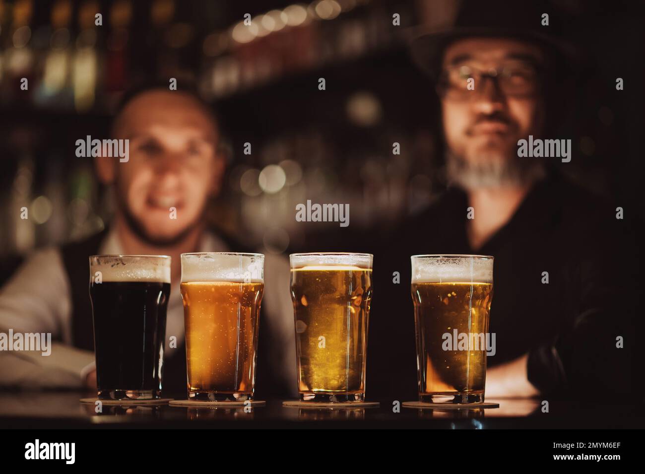 four glasses with different beers on bar counter in pub against the