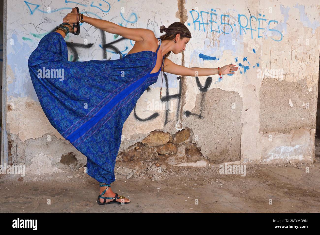 Young woman with headband does yoga exercise in old house in front of wall with graffiti Stock Photo