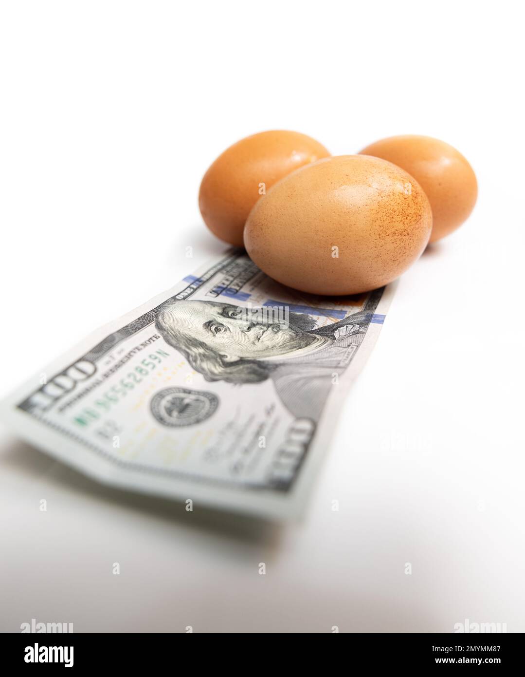 Fresh eggs on top of a 100 dollar US bill on a white background Stock
