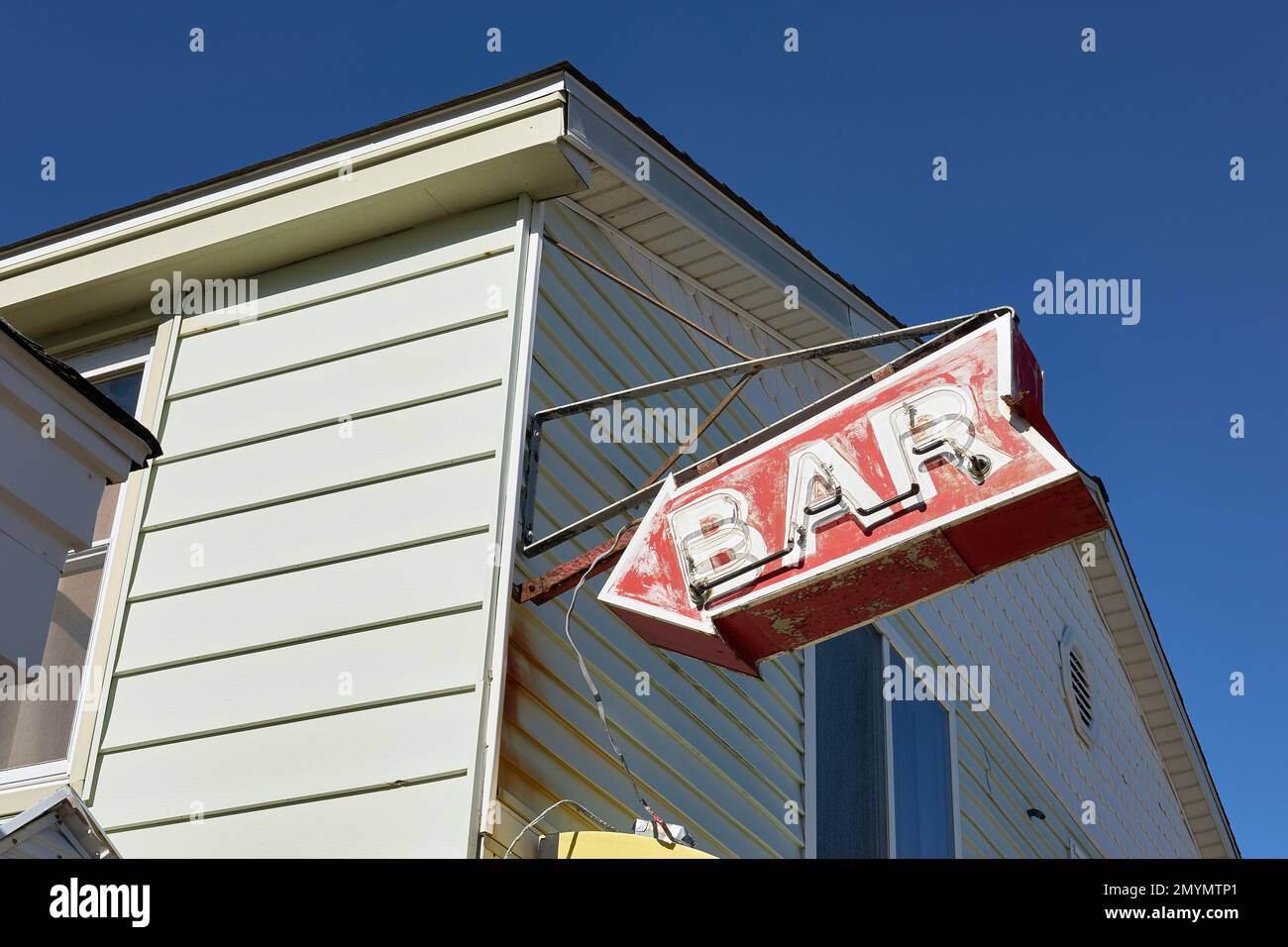 A worn, red, retro neon bar sign hang above a bove an establisment