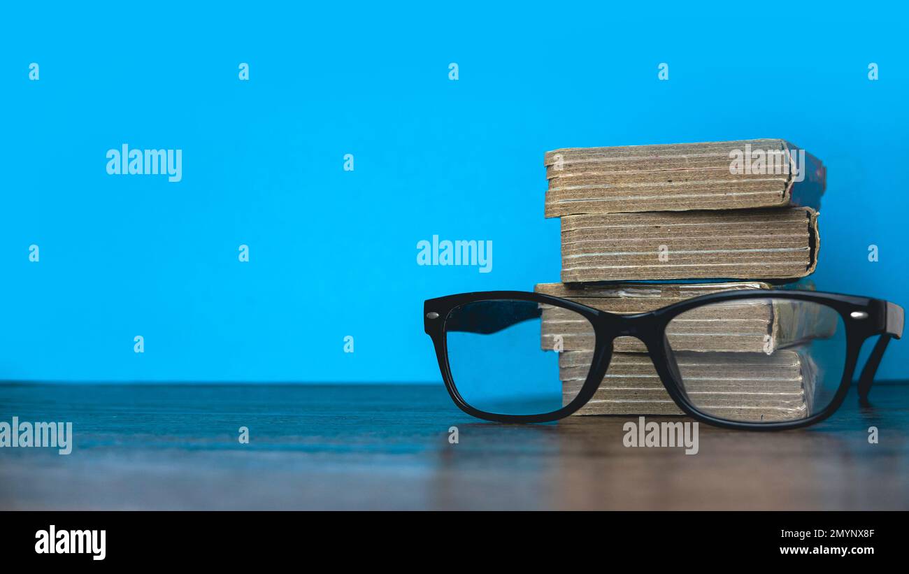 A stack of book with a glasses on a blue background with copy space. Stock Photo