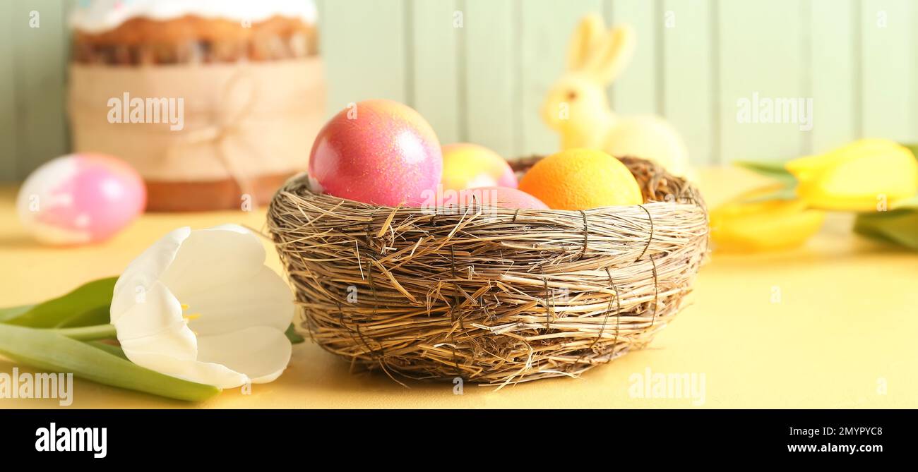 Nest with painted Easter eggs and tulip flower on table Stock Photo - Alamy