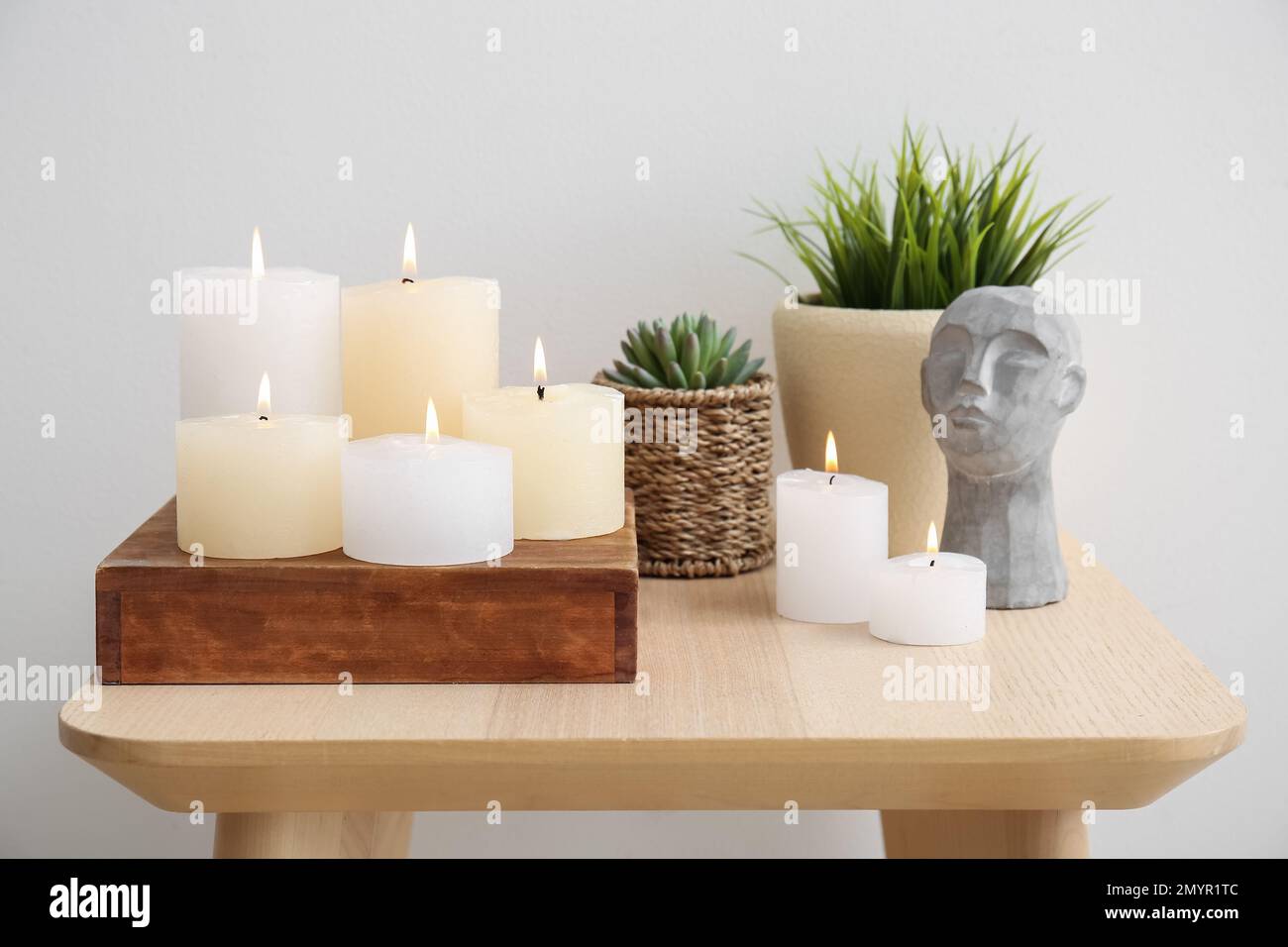 Burning candles, houseplants and decorative stone head on table near