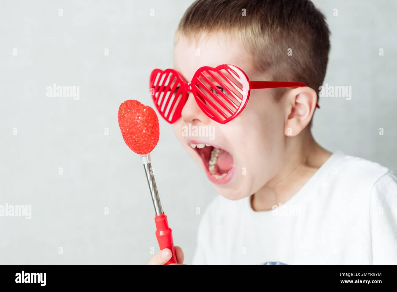 portrait of a boy in glasses in the form of a heart in a white T-shirt against a white background, screaming at the heart. Against valentine's day Stock Photo