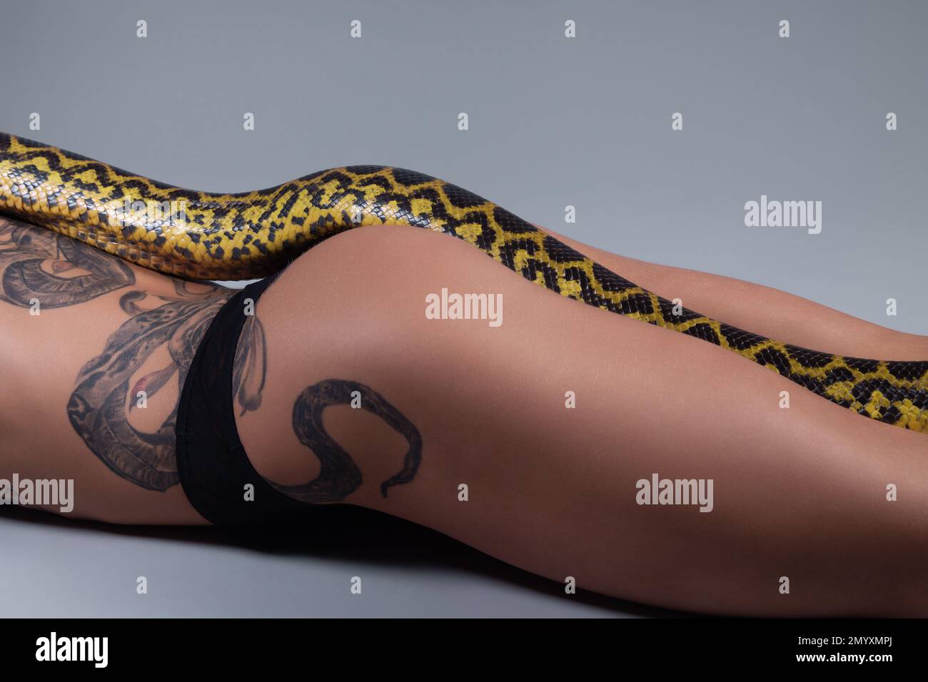 Photo of the woman lying on the floor and snake on her hips on grey background Stock Photo
