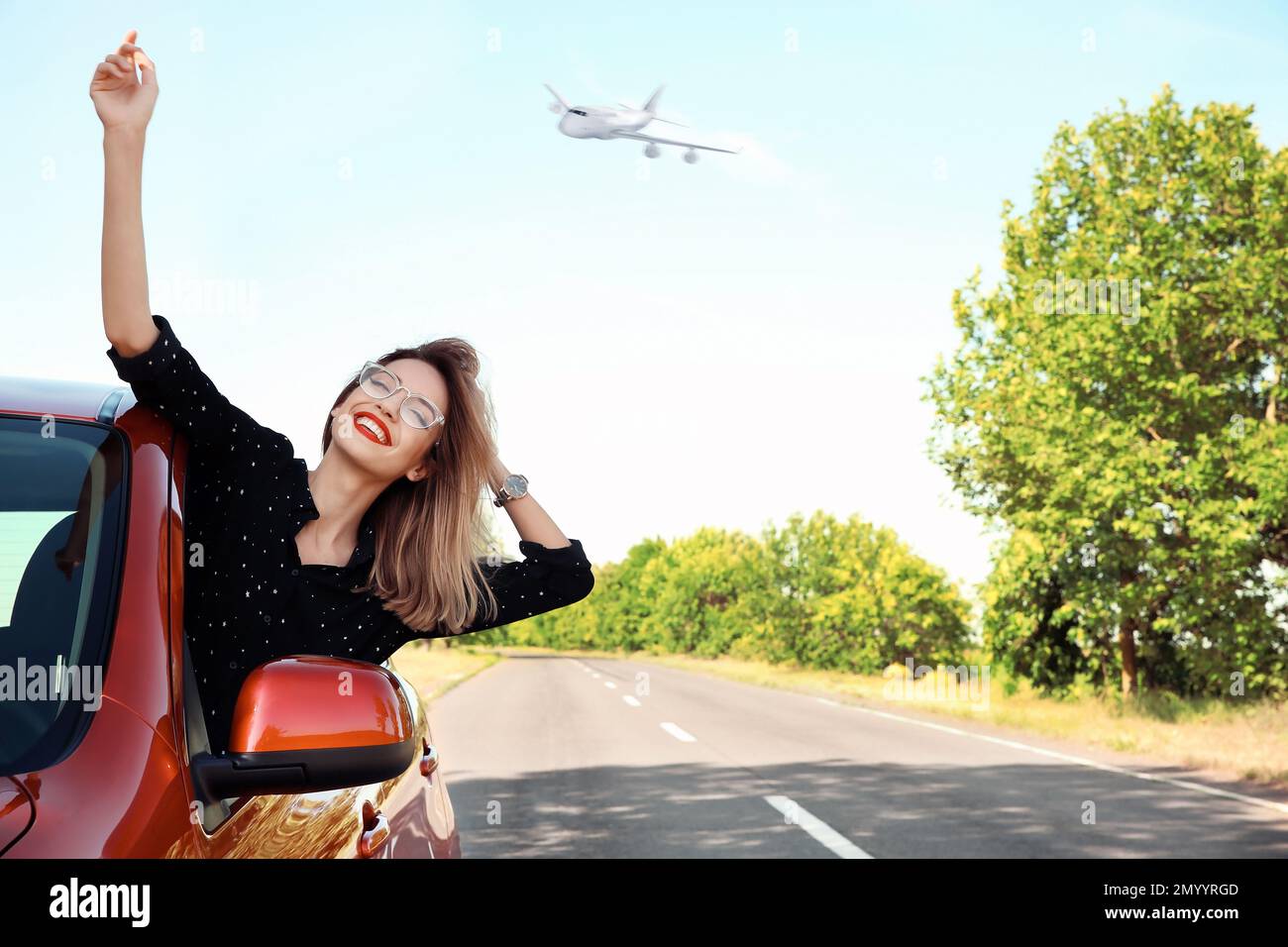 Young woman leaning out of car window and airplane in sky. Summer vacation Stock Photo