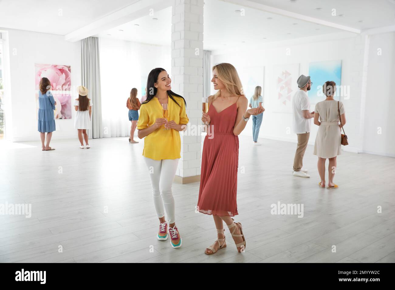 Young women with glasses of champagne at exhibition in art gallery ...