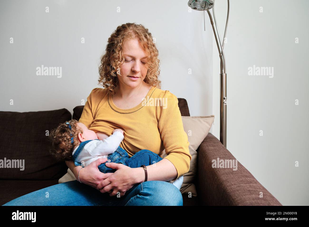 Woman breastfeeding her daughter sitting on the sofa at home. Stock Photo