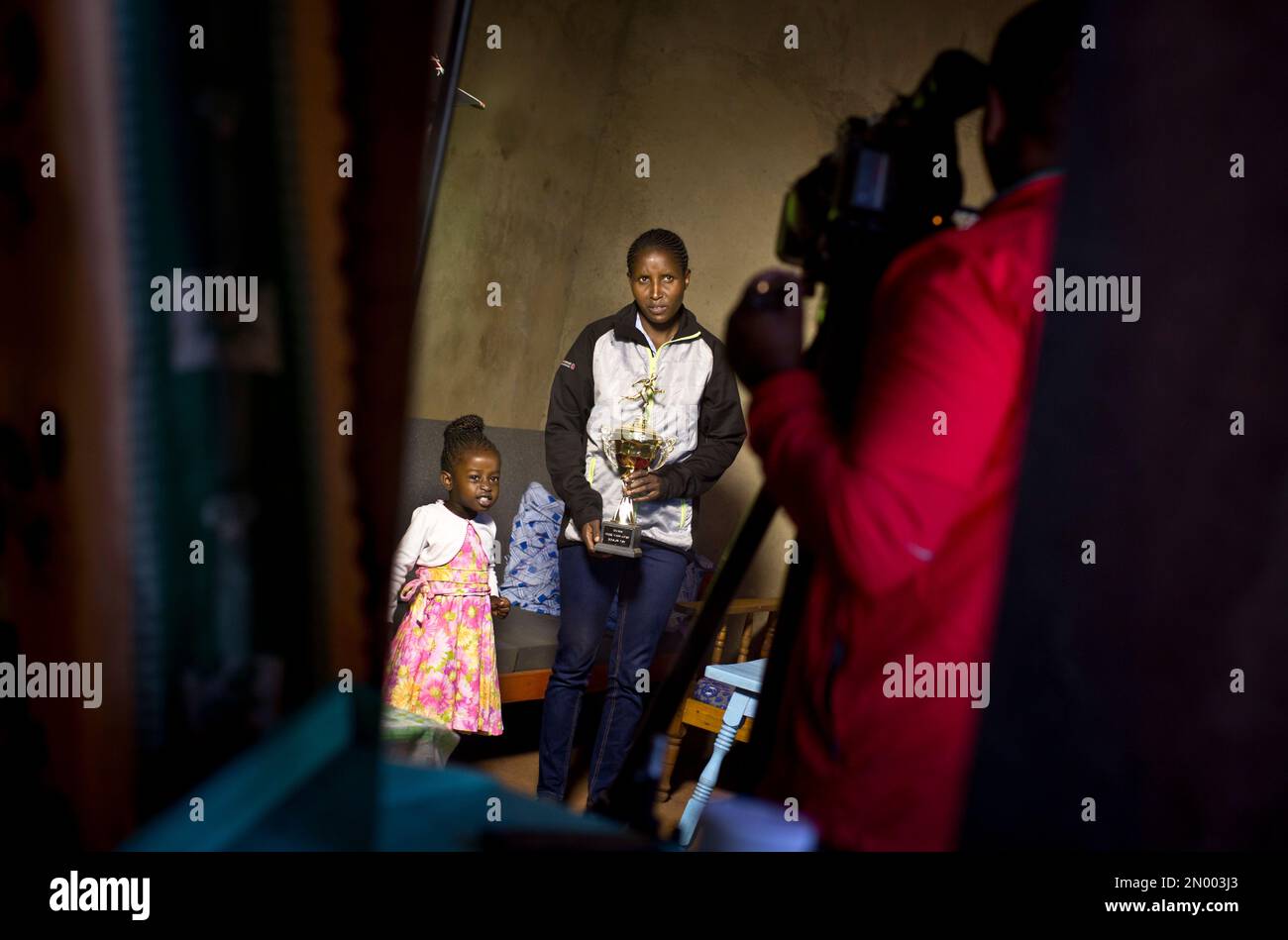 In this Monday, Feb. 1, 2016, photo, Kenyan runner Lilian Mariita, 27,  accompanied by her daughter Lisa, 2, shows one of her trophies during an  interview in her house in the village