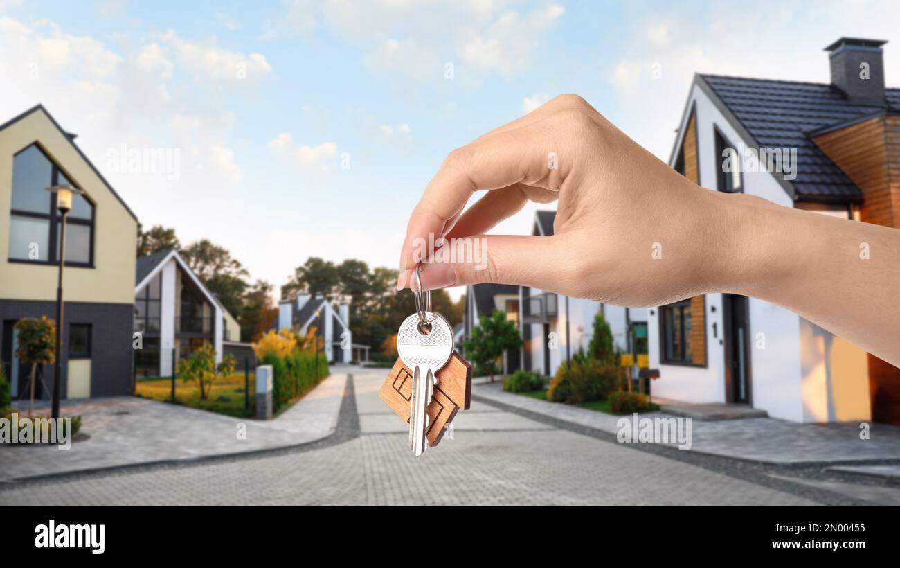 Real estate agent holding key against modern houses, closeup. Banner ...