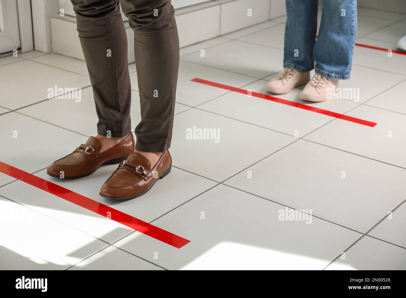 People standing in line behind taped floor markings for social distance