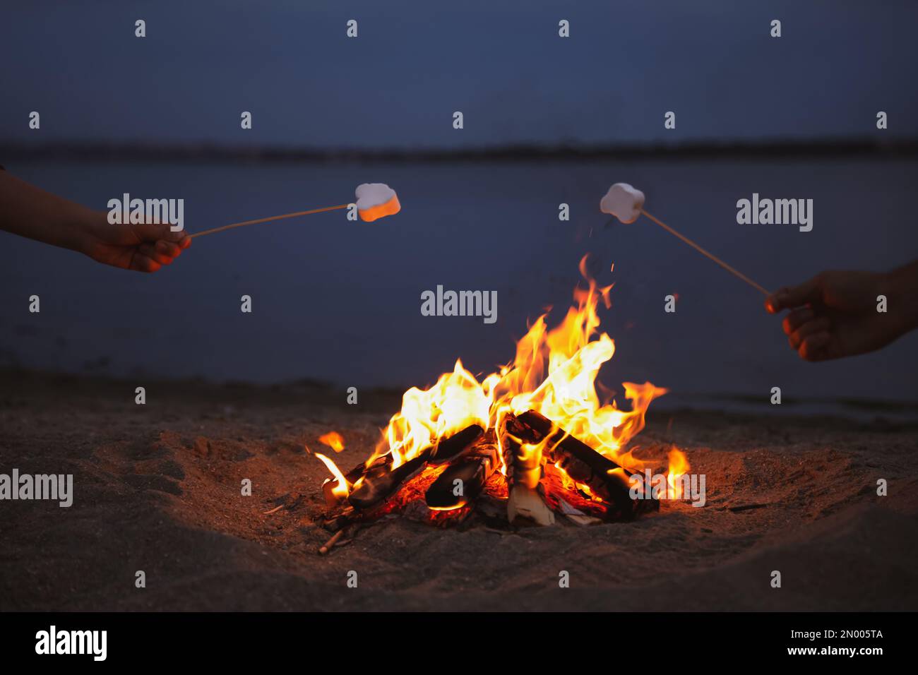 People roasting marshmallows over burning firewood on beach, closeup Stock Photo