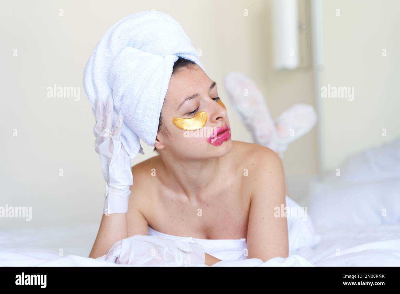 After a shower, a girl wrapped in a towel uses cosmetic patches for the
