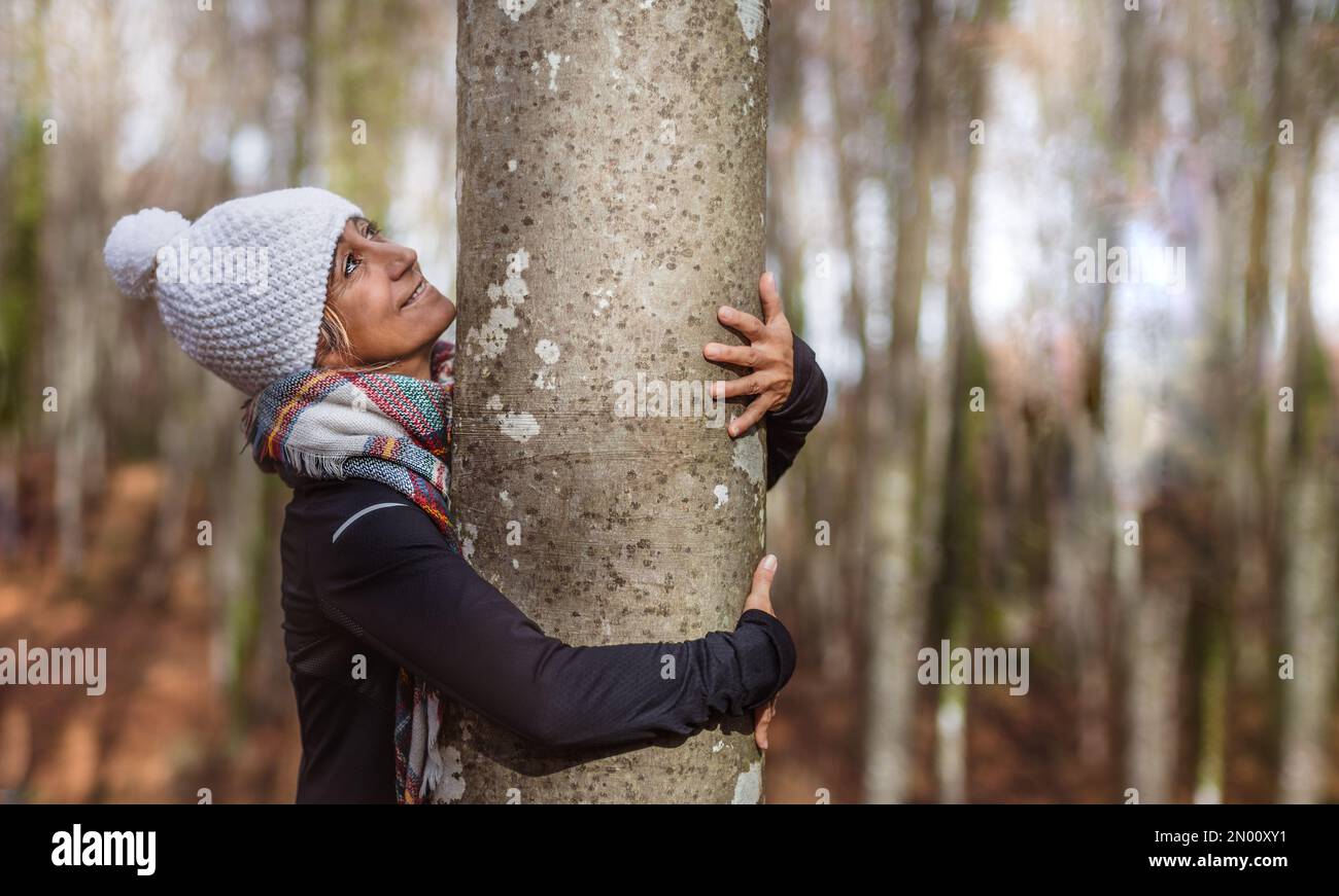 a woman in a white cap hugs a tree in a forest while looking at it with ...