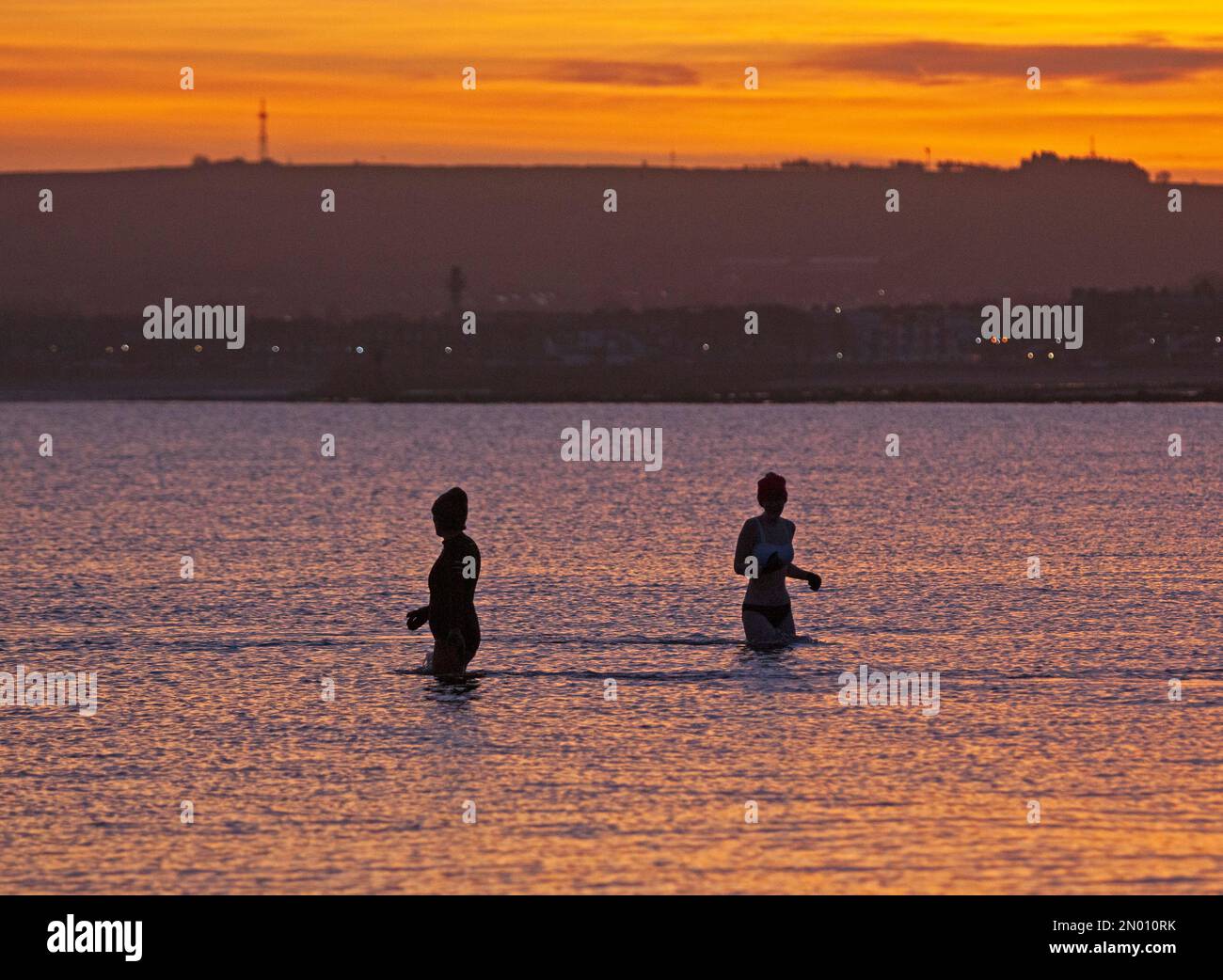 Portobello, Edinburgh, Scotland, UK 5th February 2023. Cool  colourful sky at sunrise above the Firth of Forth and seaside beach for the few people out to witness it. Temperature 1 degree centigrade with ice on wet surfaces and car windscreens. Pictured: Two cold water swimmers in the Firth of Forth for a chilly dip. Credit: Archwhite/alamy live news. Stock Photo