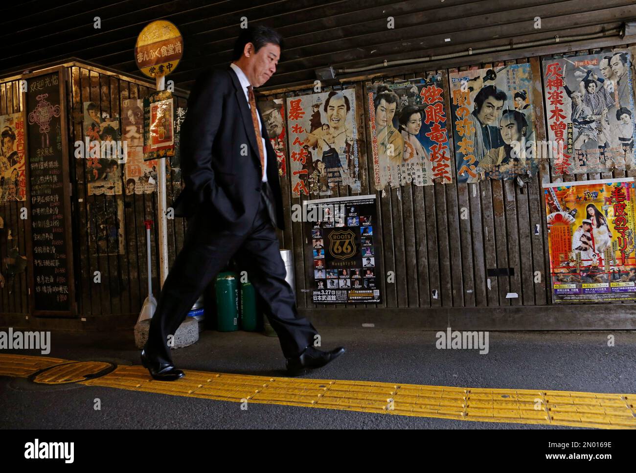 A man walks by old film posters on the wall in downtown Tokyo Thursday