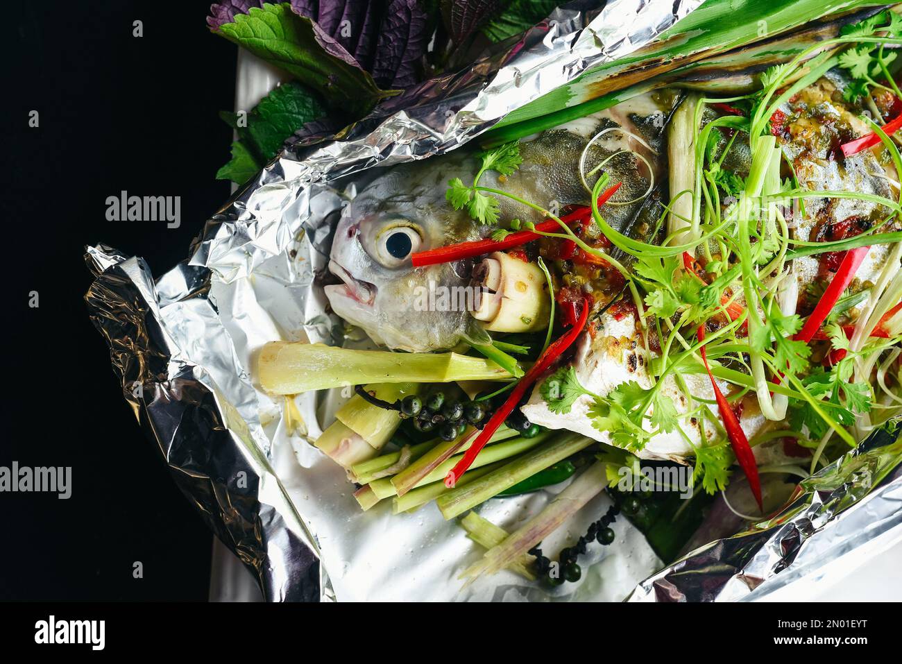 Pampus argenteus fish grilled in Vietnamese style with vegetables isolated on black background top view Stock Photo