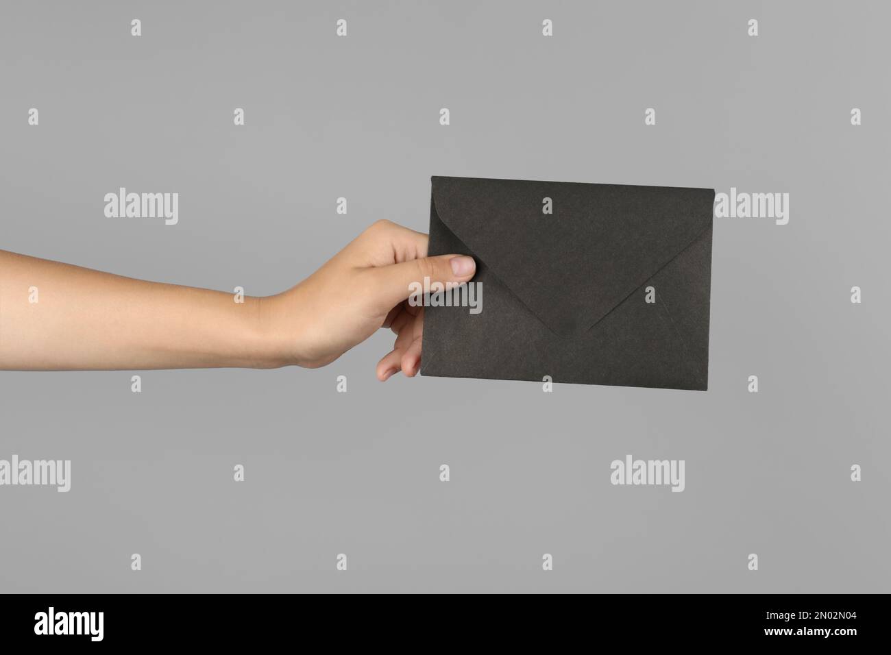 Woman holding black paper envelope on light grey background, closeup Stock Photo