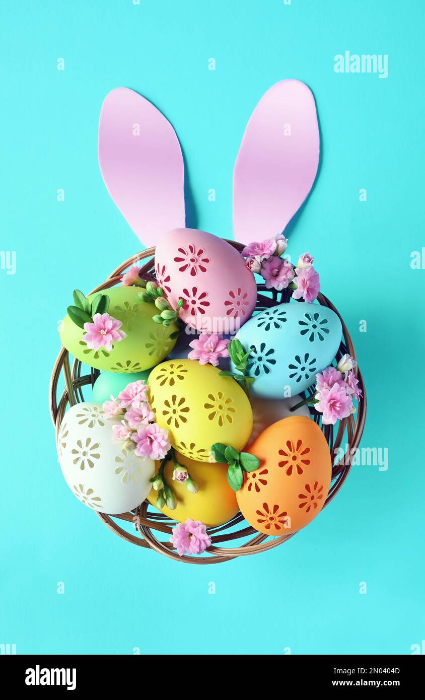 Multi colors Easter eggs in the basket with bunny ears and flowers on blue background. Pastel color Easter eggs Stock Photo