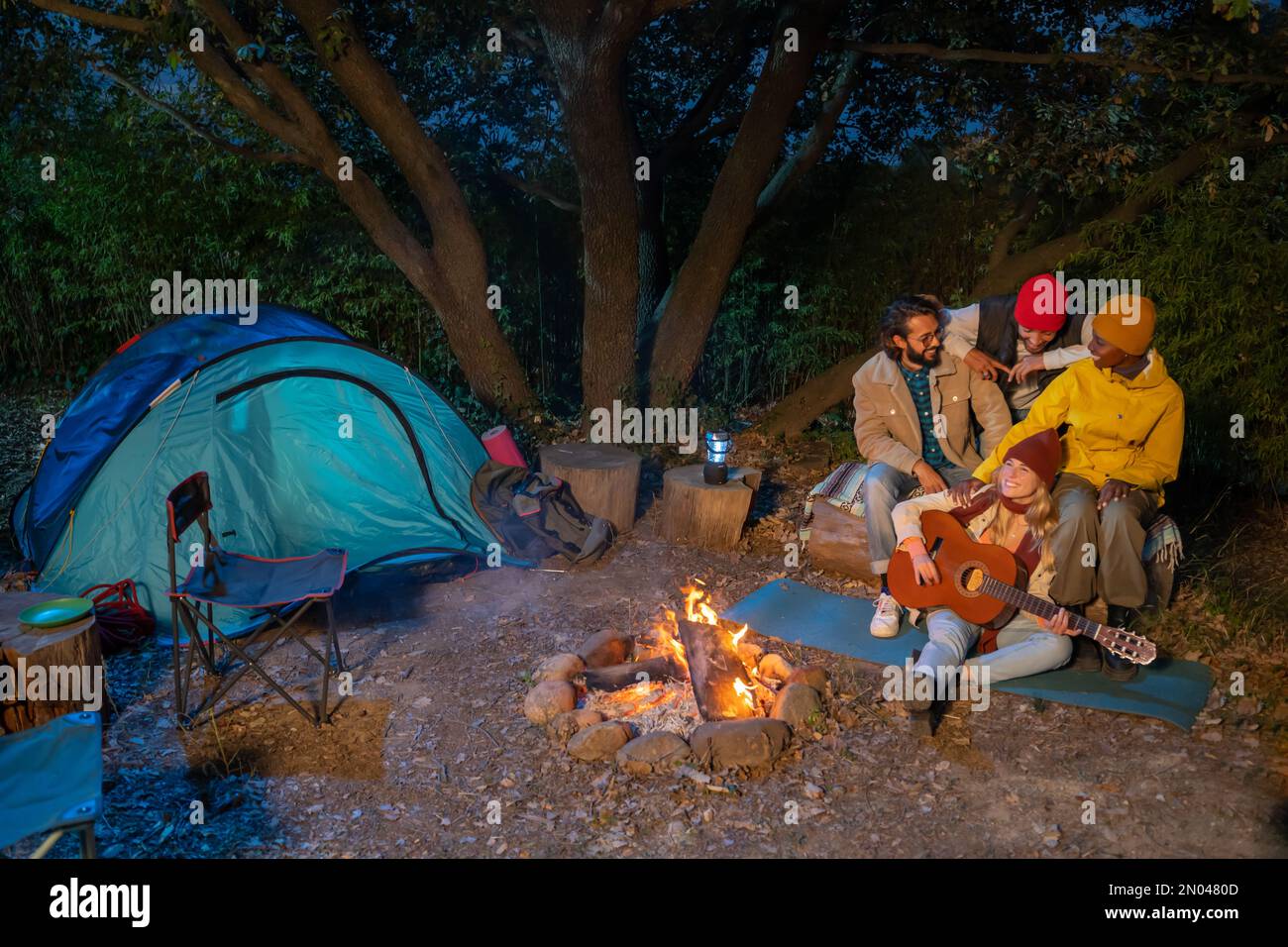 Group of friends with guitar near the bonfire and camping outdoors in the afternoon. Travel concept Stock Photo