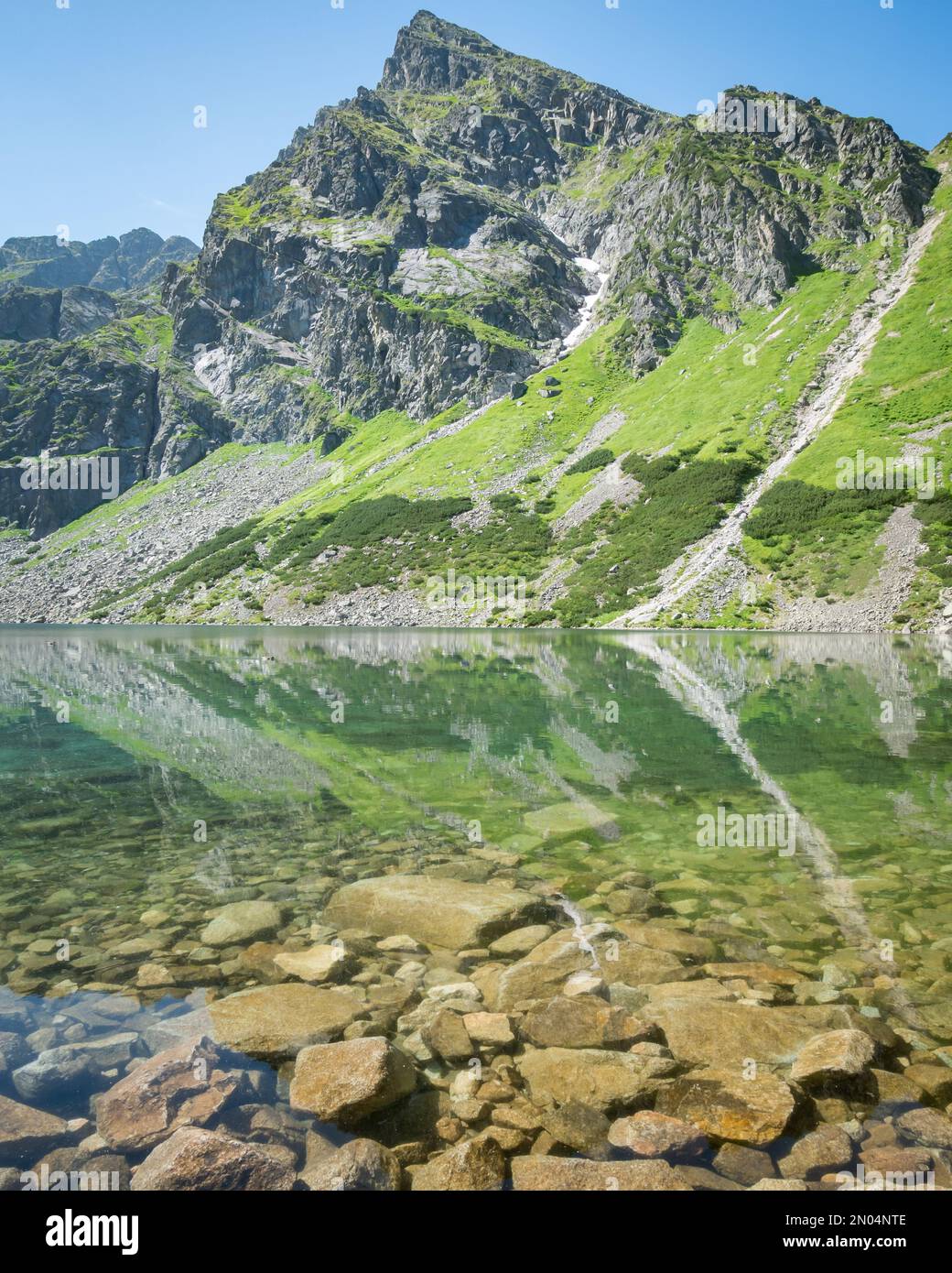 Prominent rocky mountain reflecting in crystal clear alpine lake, vertical shot, Poland, EU Stock Photo