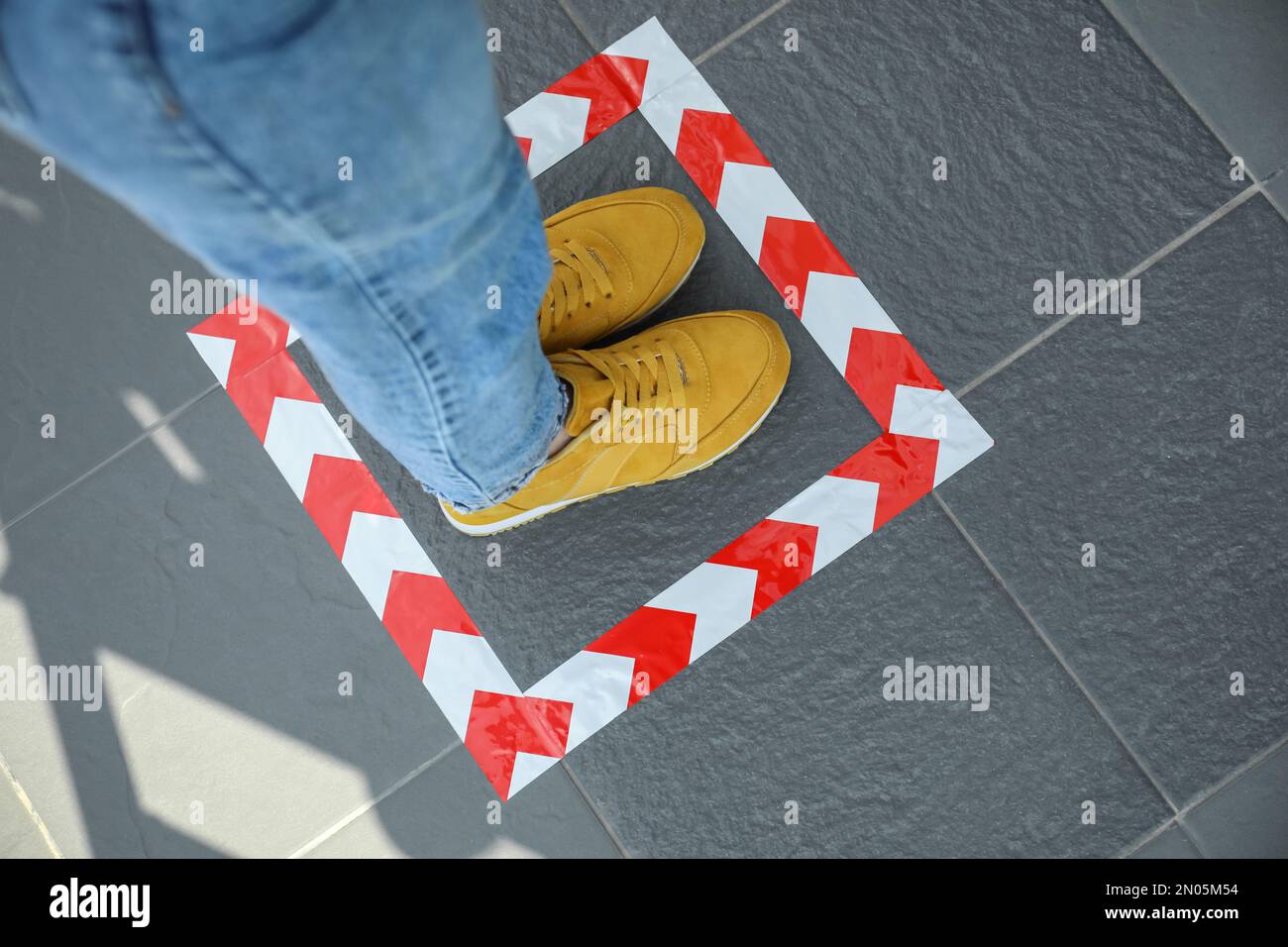 Woman standing on taped floor marking for social distance, closeup. Coronavirus pandemic Stock Photo