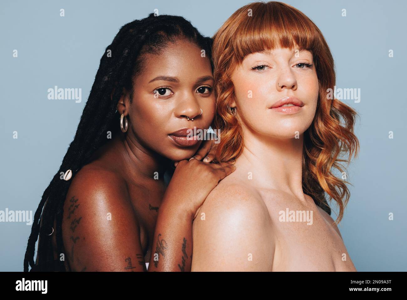 Two women with different skin tones looking at the camera while standing together. Body confident young women feeling comfortable in their own skin. D Stock Photo
