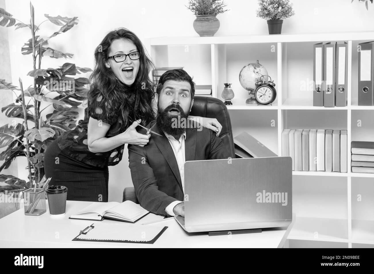 Tricky woman boss scare bearded man employee cutting beard with scissors in office, barbering